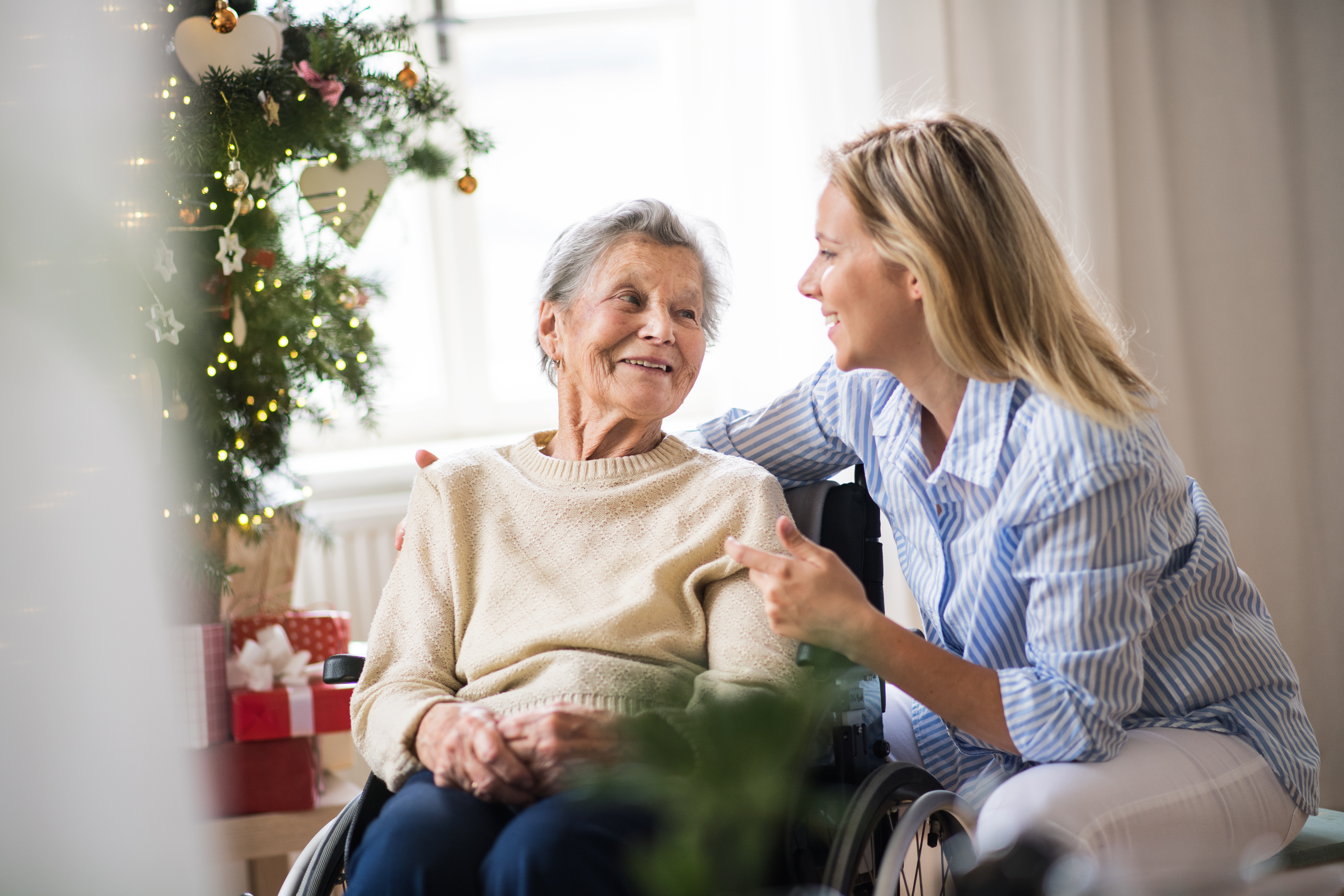 A senior women in wheelchair with a visitor near a Christmas tree.